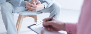 Therapist making notes while person holds hands together